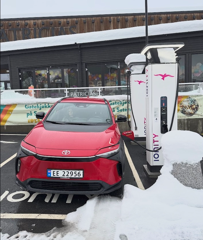 Electric vehicle at a fast charger near a café, with people eating and relaxing during the charging stop.